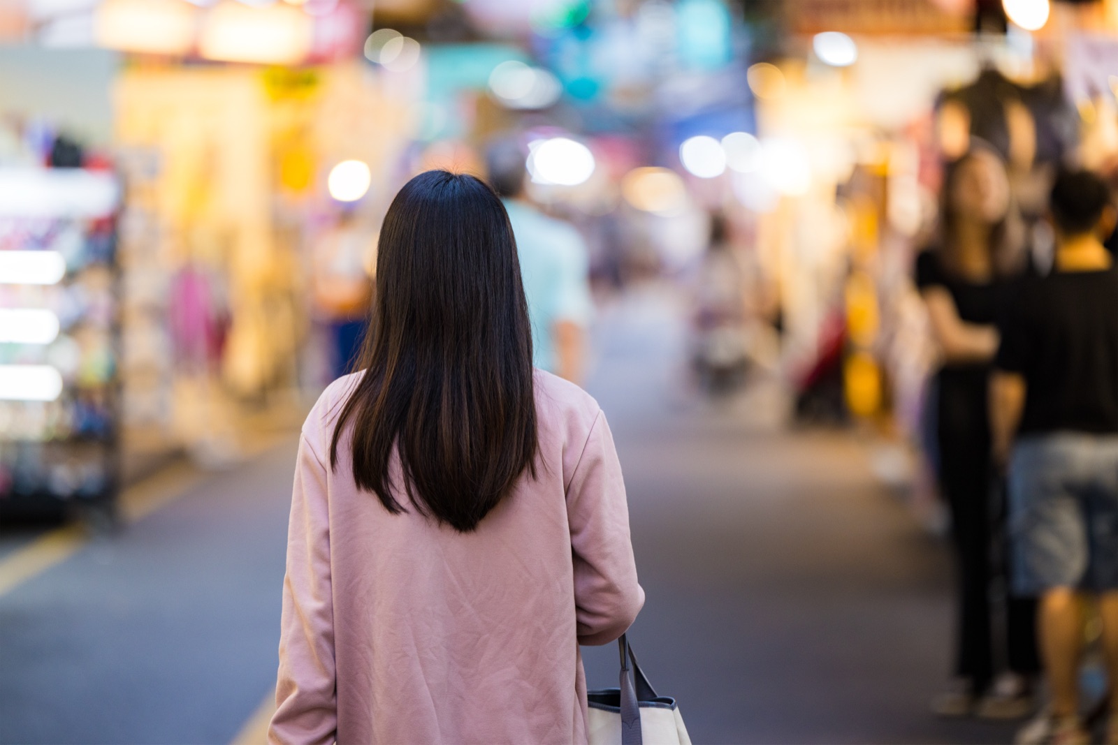 Person walking through a busy, lit-up city street market at night