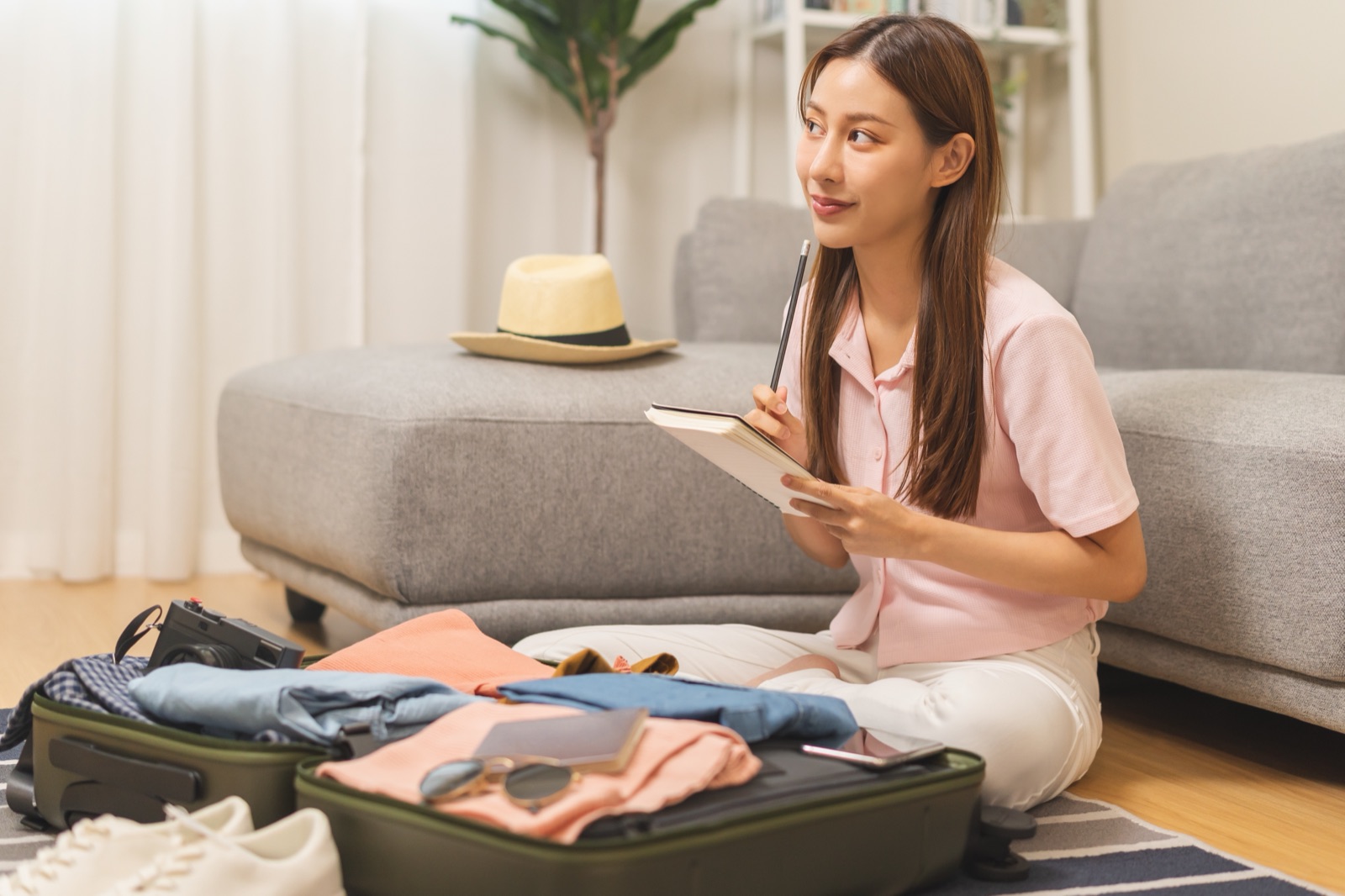 Young woman sitting on the floor with a suitcase, packing for travel